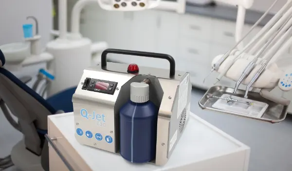Kleines medizinisches Gerät mit Aufschrift 'Q-Jet C10' und rotem Warnlicht auf einem weißen Tisch in einer Zahnarztpraxis.