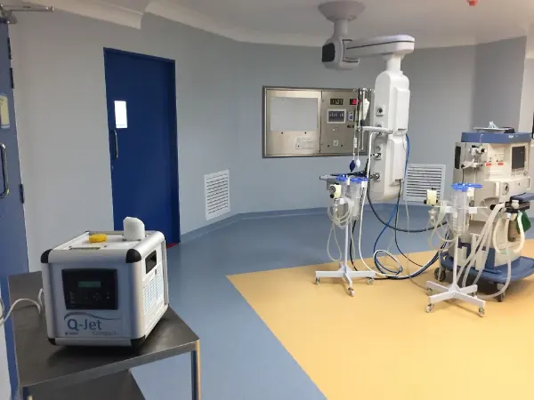 Medizinische Geräte in einem Operationssaal mit blauem und gelbem Boden, darunter ein Q-Jet-Compact-Gerät auf einem Tisch.