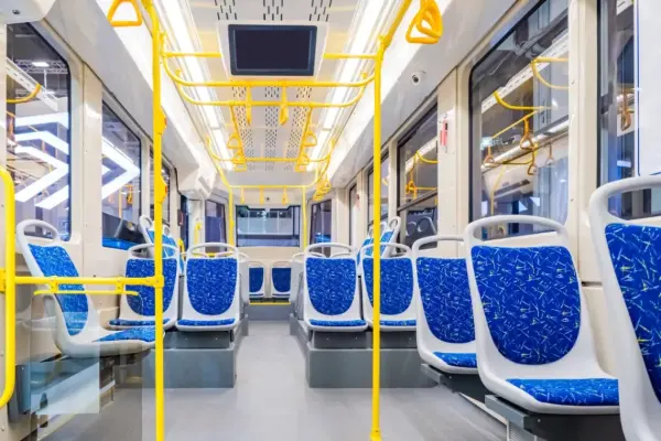 Innenansicht einer modernen Straßenbahn mit blauen Sitzpolstern und gelben Haltestangen.