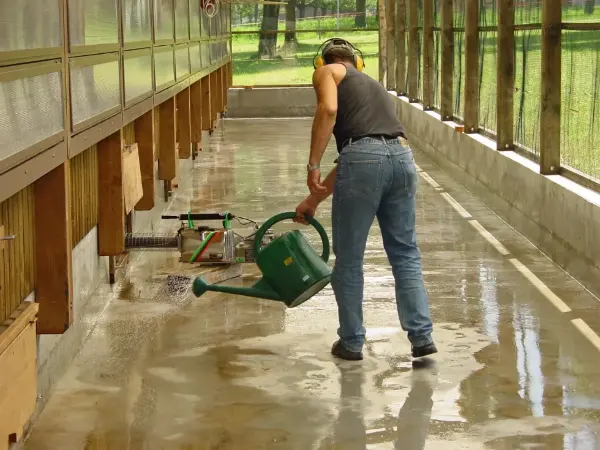 Eine Frau gießt in einem großen Innenraum manuell das Desinfektionsmittel in Tierställen anwendet.
